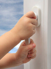 The child's hands are holding the plastic window handle. The concept of children falling out of windows in multi-storey buildings, children's safety, Cable safety guard prevent opening window by child