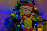 Fototapeta  - Lalka szmaciana w czapce Świętego Mikołaja . Choinka , bombki , lampki . Boże Narodzenie .