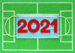 Red felt year numbers 2021 on blue medical mask placed on mini football field made of green felt, top view. Concept about soccer championship during covid pandemic. Review of the year results.