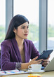 © Bangkok Click Studio - Millennial Asian female professional successful businesswoman in formal outfit sitting at work desk using touchscreen tablet computer device browsing internet website reading documents check email