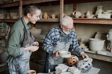 Wall Mural - Senior man showing the ceramic vases to his assistant while they working in pottery workshop