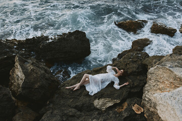 Poster - Barefoot woman Lies on his back on a stone cliff, cloudy weather view from above