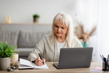 Wall Mural - Focused mature woman writing and using laptop at home