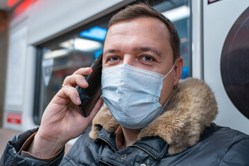 Wall Mural - Millennial man in medical mask making a phone call in a subway train. Happy mature guy commuting to work on train using mobile phone. new normal concept during pandemic coronavirus