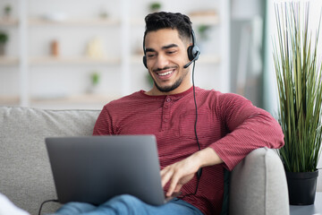 Happy arab guy attending online webinar, using laptop and headset