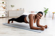 © Prostock-studio - Sports and weight loss concept. Overweight African American woman doing exercises on mat at home, full length