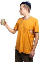 A Homeless Man Looks Away, Holds A Can Of Canned Food, An Orange Torn T-shirt. Isolated White Background