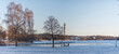 Panorama view over the bay Djugårdsbrunsviken, a bench and a lamppost at a view point from a snowy meadow and a skyline with the tele tower Kaknästornet a winter day afternoon in Stockholm