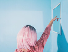 Woman With Pink Hair Pointing At Mirror On Blue Wall