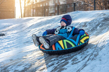 A Happy Child With His Mother Is Tubing With A Park From A Slide. A Fun Winter Weekend In The Park Outside