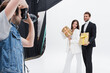 © LIGHTFIELD STUDIOS - blurred photographer taking picture of smiling models with gift boxes on white.