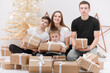 Holidays Concept. cute teenagers are sitting by the wooden decorations Christmas tree and many gift boxes. three brothers and sister having fun on New Year's Eve