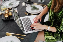 Cropped Image Of Woman In Green Dress Using Computer Sitting At A Dinner Table