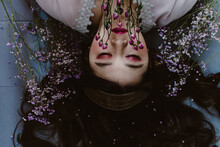Upside Down Photo Of Woman With Pink Makeup Laying On The Ground Next To Pink Flowers
