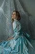 © Scopio - Woman in long blue dress sitting on floor beside light curtain