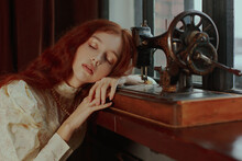 Young Woman With Red Hair Leaning Her Head Sleeping Beside Sewing Machine