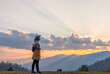 Travel young girl with backpack and hat enjoying sunset on peak mountain