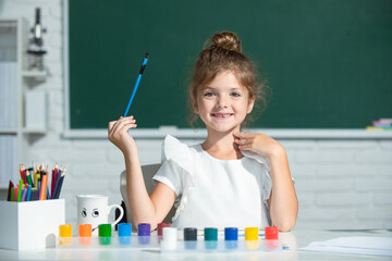 Kids creative growth. Child girl draws in classroom sitting at a table, having fun on school blackboard background.