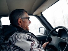 An Elderly Man In A Winter Jacket Drives A Lada Car In Winter On A Fishing Trip. He Is Nervous And Screams, As It Is Winter And Snow Behind The Glass Of The Windows.