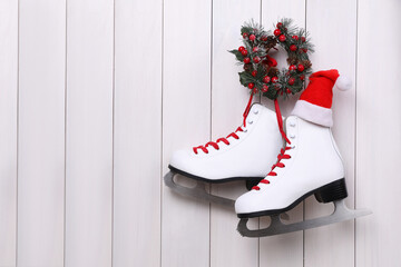 Poster - Pair of ice skates and Christmas wreath hanging on white wooden background, space for text