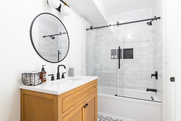 A beautiful bathroom with a wood vanity, custom tile shower and floor, and a sliding glass door with black hardware.