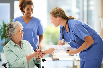 shot of an attractive female nurse holding medical records while shaking hands with her wheelchair-b