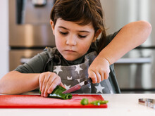 Little Girl Cutting Green Pepper In Kitchen