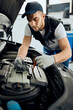 © Drazen - Young mechanic checks oil level while maintaining car engine at auto repair workshop.