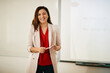 © Drazen - Happy female teacher stands in front of whiteboard in classroom and looks at camera.