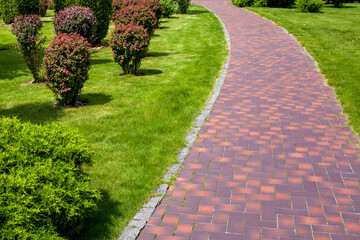 Wall Mural - curved stone tile pavement curved path in park landscaped with green grass and foliage bushes, garden landscape design of backyard on a sunny summer day, nobody.