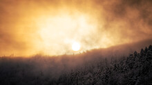 The Sun Shimmers Through The Clouds Over A Mountain Ridge In The Black Forest