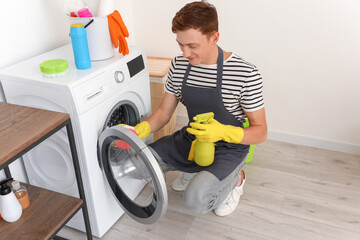 Handsome man cleaning washing machine with sponge in bathroom