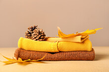 Stack Of Baby Clothes, Pine Cones And Autumn Leaves On Color Background