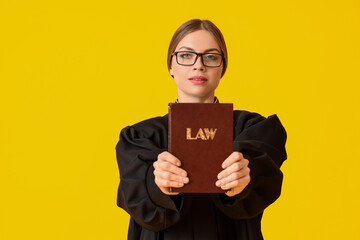 Wall Mural - Young female judge with book on color background