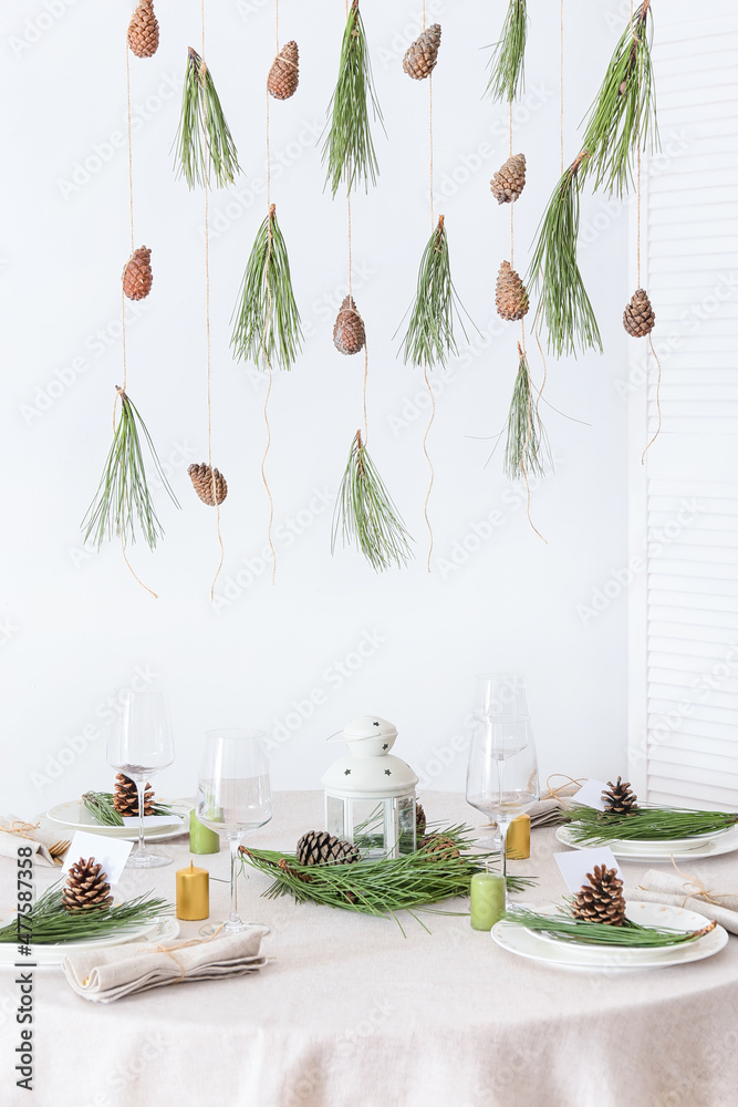 Beautiful table setting with pine cones and fir branches near white wall