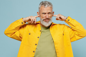 Elderly gray-haired mustache bearded man 50s in yellow shirt cover ears with hands fingers do not want to listen scream isolated on plain pastel light blue background studio People lifestyle concept