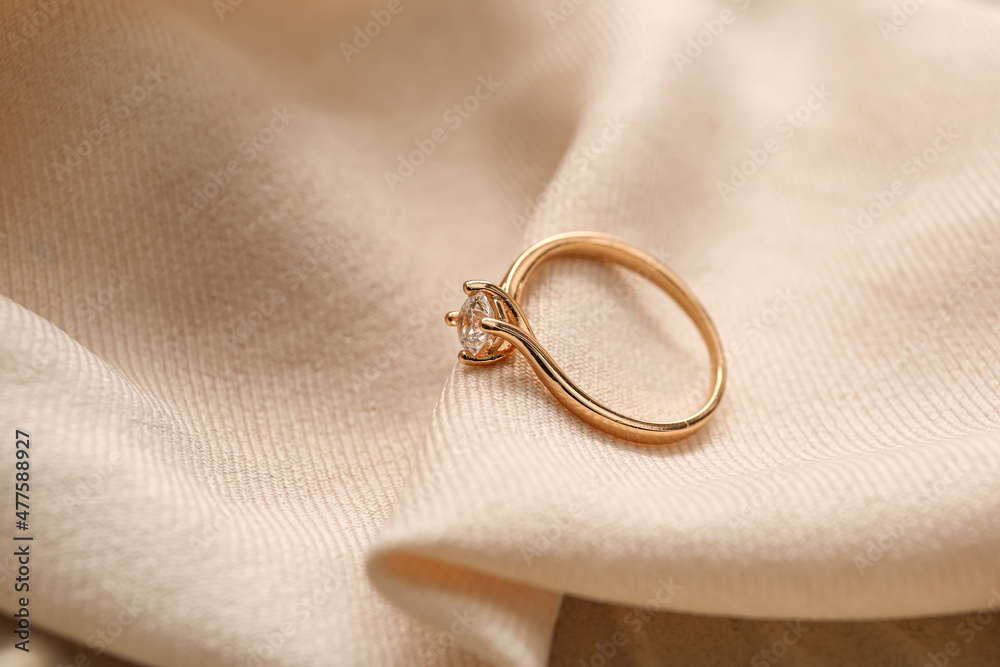 Golden engagement ring on beige fabric background, closeup