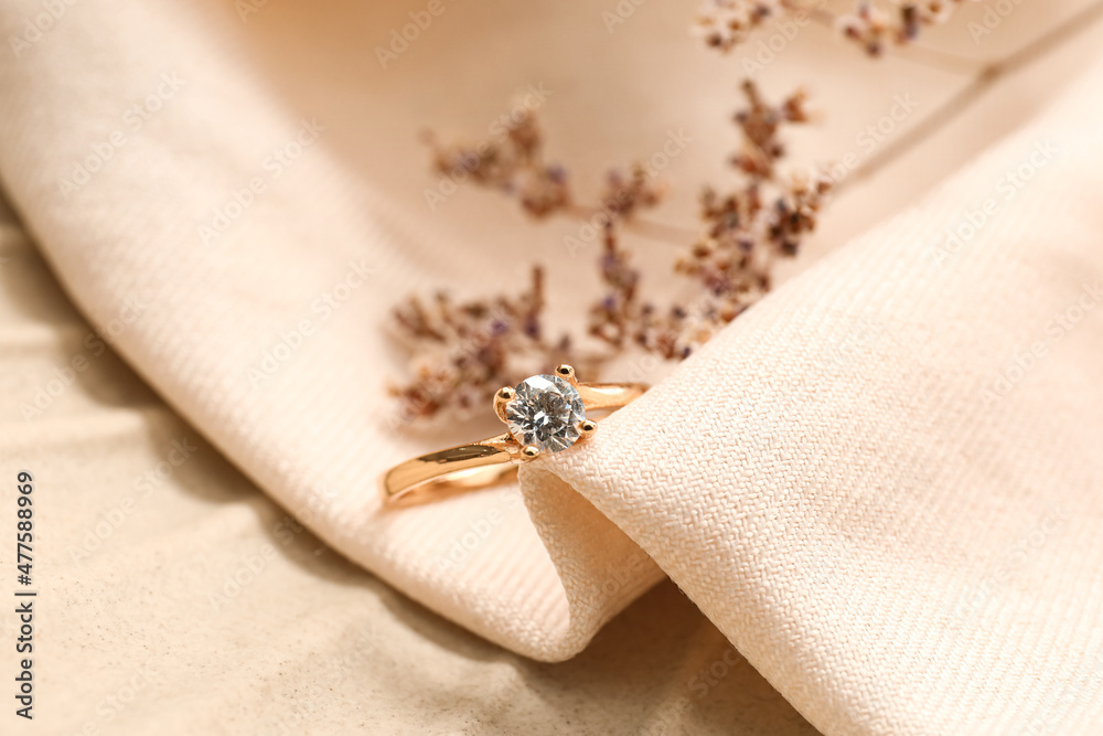 Golden engagement ring with flowers on beige fabric background, closeup