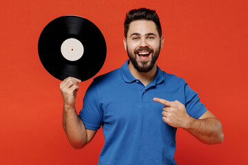 Wall Mural - Young excited happy satisfied amazed cool fun man 20s in basic blue t-shirt point finger on hold retro vintage music plate isolated on plain orange background studio portrait People lifestyle concept