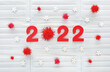 Red felt year numbers 2022 on light blue medical masks background. Zero is fluffy pompon as a coronavirus molecule. Wooden white snowflakes and red pompons around. Covid-19 pandemic year results.