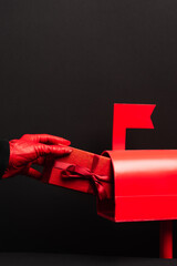 Canvas Print - cropped view of person in red glove putting wrapped present in post box isolated on black.