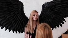 Kyiv, Ukraine - December 18, 2021: Photographer Corrects The Hair Of A Model With Black Angel Wings At A Photo Shoot.