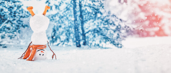 Wall Mural - Cheerful snowman with orange scarf and in yellow boots stands upside down in winter