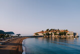 Fototapeta  - Sandy beach with sun loungers and umbrellas leading to Sveti Stefan Island