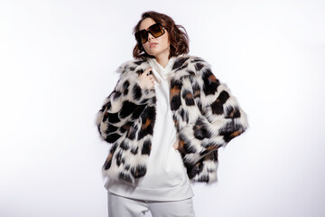 High fashion photo of beautiful elegant young woman in a pretty leopard print fur coat, stylish sunglasses, trousers, pants, black sneakers posing on white background. Make up, hairstyle. Slim figure