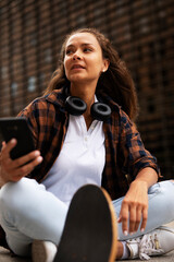 Wall Mural - Fashion woman with skateboard. Young happy girl using the phone. Beautiful woman enjoy outdoors