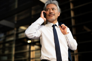 Wall Mural - Senior businessman outdoors. Middle-aged businessman talking to the phone. Handsome man in suit using the phone.