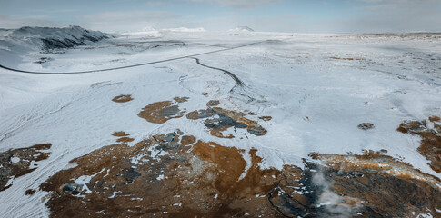 Wall Mural - Aerial Drone panorama with hot steam coming from the ground. Hverir is geothermal area in Myvatn. Landscape covered with snow and orange ground.