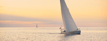 White Sloop Rigged Yacht Sailing In The Baltic Sea At Sunset. Clear Sky After The Storm, Golden Sunlight. Transportation, Travel, Cruise, Sport, Recreation, Leisure Activity, Racing, Regatta