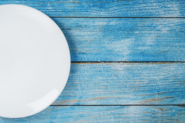 An empty round white plate on a blue wooden table.